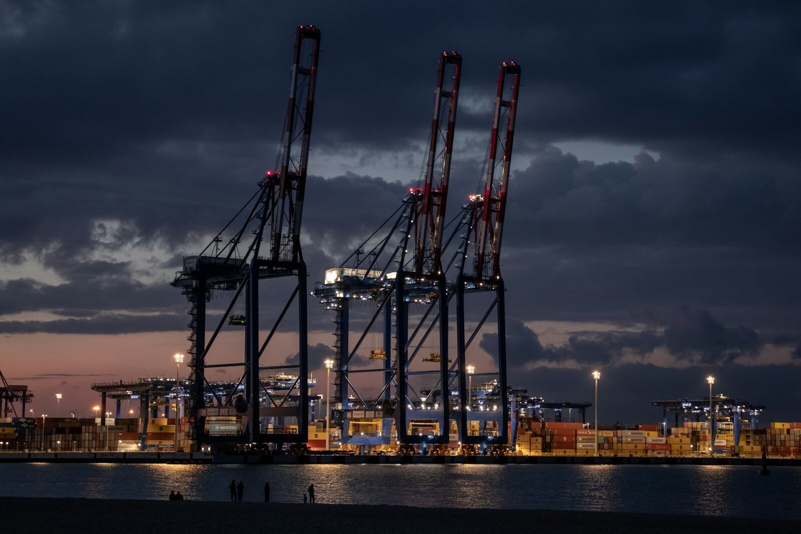 Harbor cranes at dusk with city lights